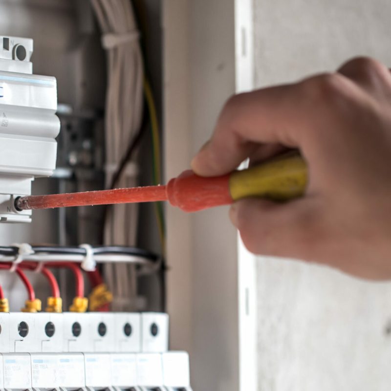 Man, an electrical technician working in a switchboard with fuses. Installation and connection of electrical equipment. Close up. Man, an electrical technician working in a switchboard with fuses. Installation and connection of electrical equipment. Professional with tools in hand. concept of complex work, space for text.